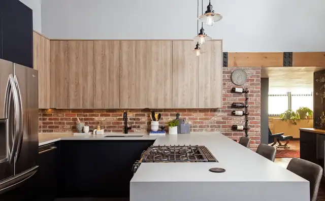 South Loop loft condo kitchen with light wood upper cabinets, navy base cabinets, a white quartz peninsula and exposed brick