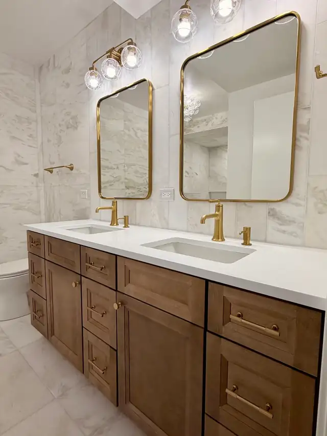 Chicago guest bathroom remodel with marble-look wall tile, wood double vanity, brass-framed mirrors and brass faucets