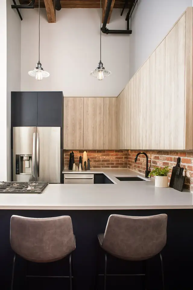 South Loop Chicago loft kitchen with exposed ceiling beams, glass pendants, peninsula seating and stainless refrigerator